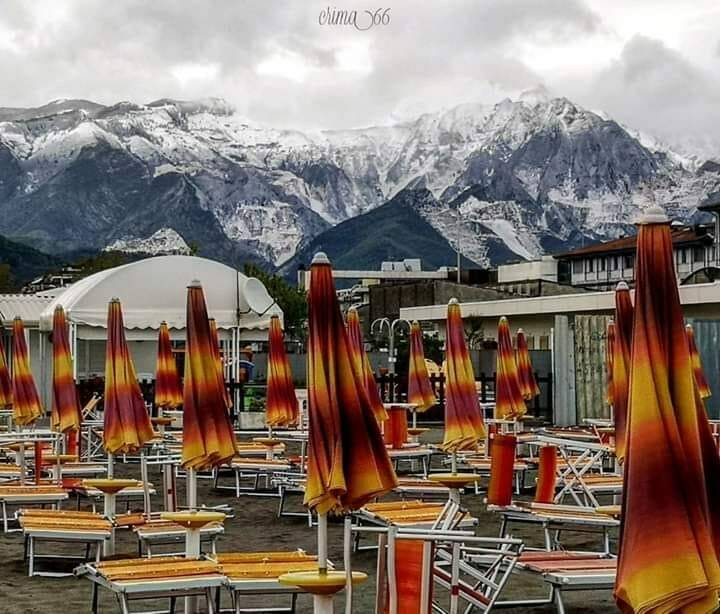 Ombrelloni sulla spiaggia di Marina di Carrara e neve sulle Apuane